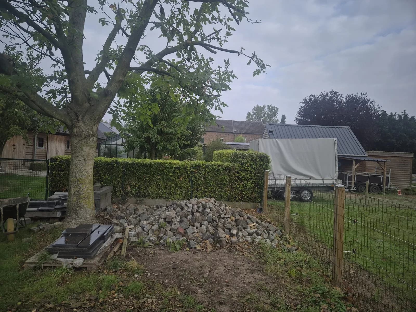 Hoop kasseien en puin naast een haag en tuinhuis, voor de ontruiming in Limburg